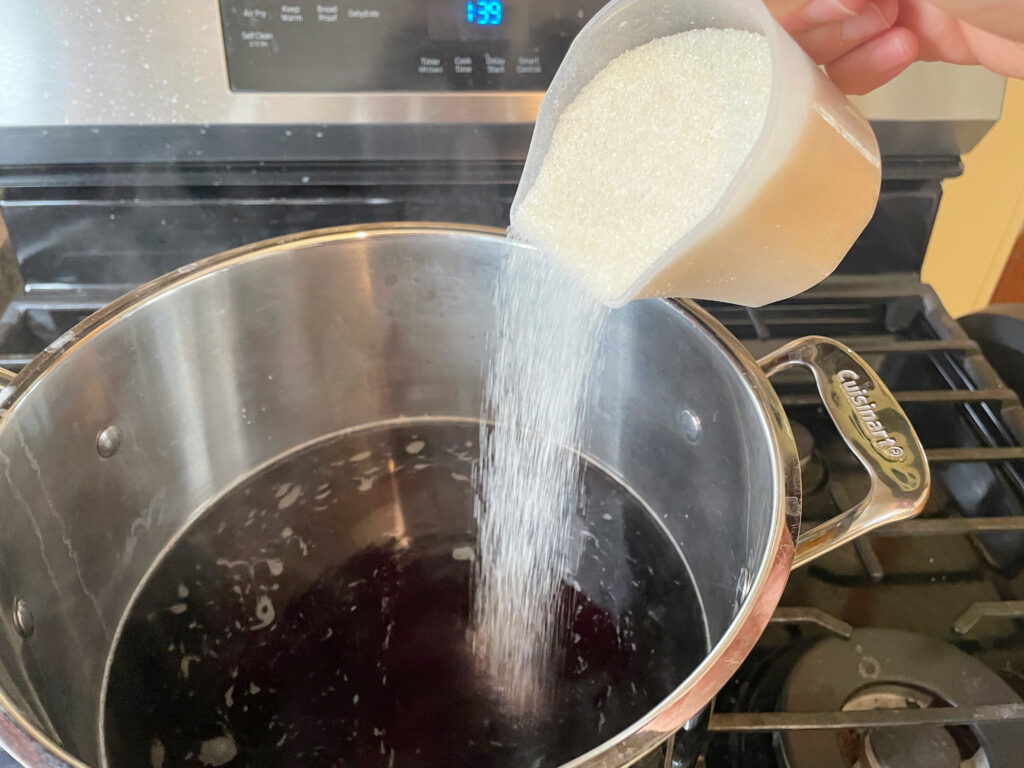 sugar being poured into pot of tea for kombucha on stove