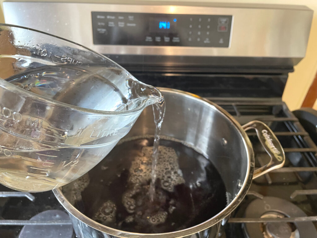 tea in pot on stove with water being poured in to make kombucha