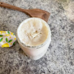 sourdough starter in glass jar next to wooden spoon and jar topper