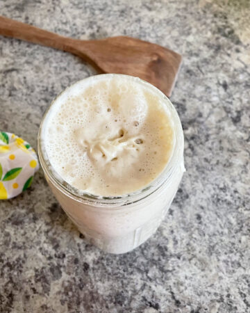 sourdough starter in glass jar next to wooden spoon and jar topper